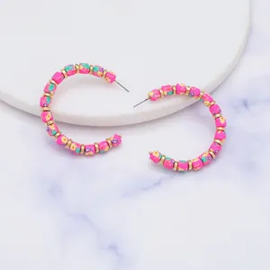 Gedetailleerde close-up van boho roze polymeer klei kraal creolen met gouden accenten.
