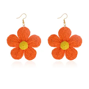 Handgemaakte raffia geweven bloem oorbellen detailopname, levendig oranje gele zomer vakantie stijl.