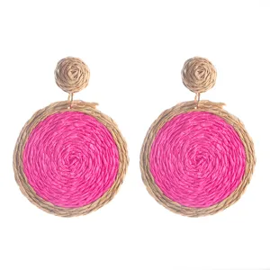 Gedetailleerde close-up van handgemaakte strooien oorbellen met een rond roze en beige design.