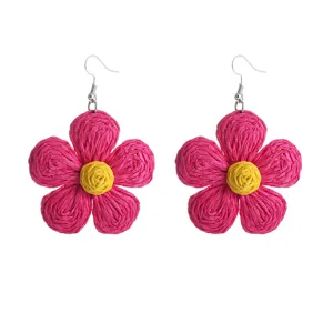 Close-up van handgemaakte raffia geweven oorknopjes met roze bloemblaadjes en geel hart.