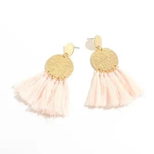 Pink tassel drop earrings detail showing the textured gold metal disc and delicate fringe.