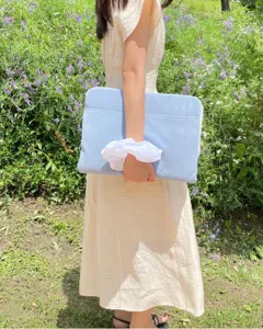 Detailed shot of light blue corduroy laptop sleeve held by model outdoors in scenic green field