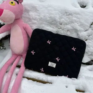 Black quilted laptop sleeve featuring cute pink bow embroidery, detailed texture view.