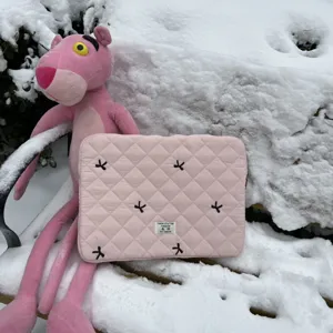 Pink quilted laptop sleeve detail, cute black bow embroidery, cozy outdoor snow background.