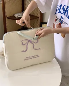 Detailansicht der niedlichen beige Laptoptasche mit lila Schleifenstickerei und Griffdesign.