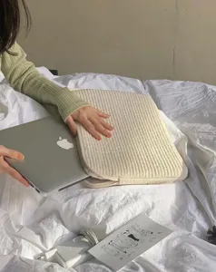 Detailaufnahme der gesteppten Laptoptasche auf einem gemuethlichen Bett, minimalistisch.