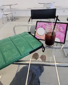 Primo piano della custodia trapuntata verde per laptop su tavolo di vetro in stile caffè.