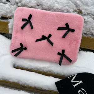 Pink plush laptop sleeve detail, cute black bow decorations on soft furry surface, cozy winter style.