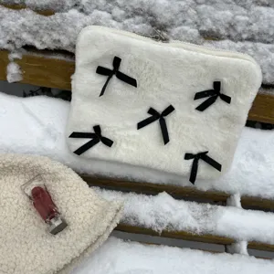 Detailed shot of the white plush laptop sleeve featuring cute black bows on snowy outdoor bench.