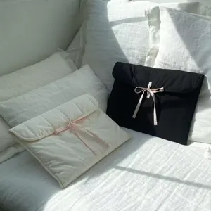 Nahaufnahme von gesteppten Laptoptaschen mit zarter rosa Schleife in Weiss und Schwarz.