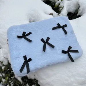 Detailed close-up view of fluffy light blue laptop sleeve featuring cute black bows outdoors.