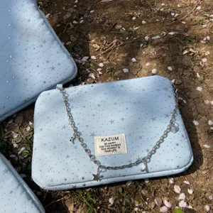 Light blue laptop sleeve detail with silver stars, metal chain charms and brand fabric label.