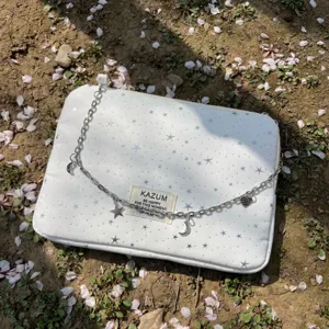 Detailed view of white laptop sleeve with silver stars, metal chain and charm, outdoor setting