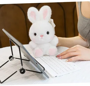 Cute white plush bunny toy detail shot on office desk with keyboard and tablet stand.