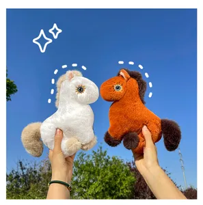 Close up detail view of cute plush horse toys held against clear blue sky outdoor background.