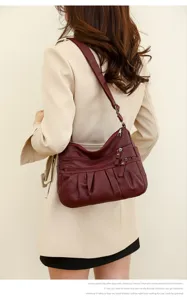Detailed view of women's burgundy soft leather shoulder bag with multiple zippered pockets.