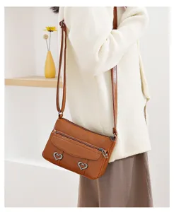 Brown leather crossbody bag detail, soft PU leather with metal heart decor and zipper.