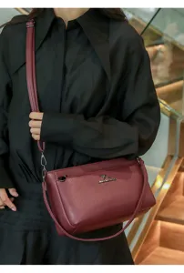 Detail view of wine red soft leather crossbody bag with metal kangaroo logo and adjustable strap.