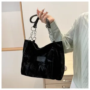 Detail view of black velvet tote bag with metal chain strap and front patch label.