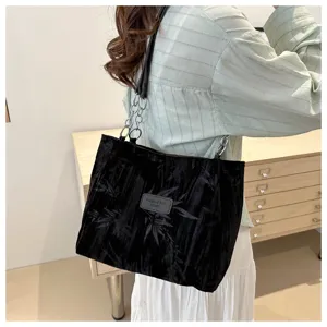 Detail view of black velvet tote bag showcasing metal chain straps and brand label patch.