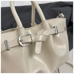 Close-up detail of trendy off-white bucket bag featuring elegant buckle strap and hardware.