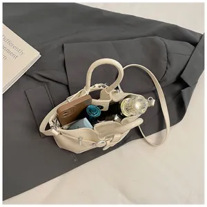 Detail view of a chic beige bucket handbag filled with daily essentials on a dark fabric backdrop.