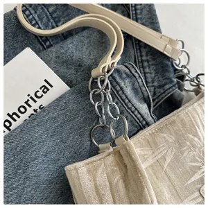 Detail view of a stylish beige velvet shoulder bag with chic metal chain and leather straps.