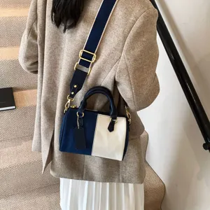 Detail shot of blue and white colorblock denim Boston bag with wide shoulder strap on model.