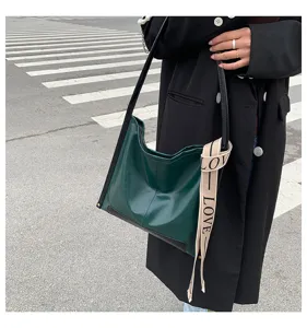 Dettaglio borsa a tracolla verde con pregiata trama in pelle e nastro elegante.