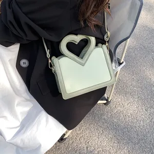 Detailaufnahme einer stylischen grünen Umhängetasche mit Herz-Griff im Freien präsentiert.