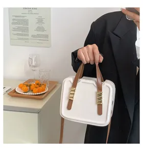 Close-up detail view of the fashionable contrast color biscuit handbag with chic brown handles.