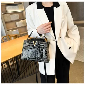 Detail view of elegant crocodile pattern handbag with gold V hardware and top handle.