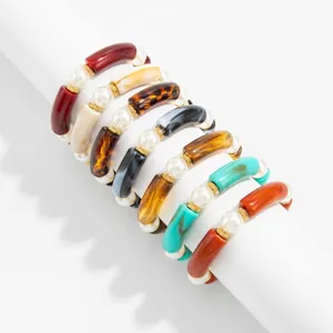 Detail of multi-colored curved tube bead bracelets with white pearls on a white display stand.