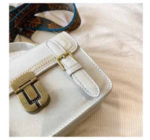 Detailopname van witte vintage schoudertas met metalen slotgesp en geborduurde lijn.