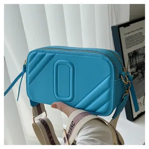 Gros plan détaillé du sac photo élégant en cuir bleu avec motif matelassé et large sangle.