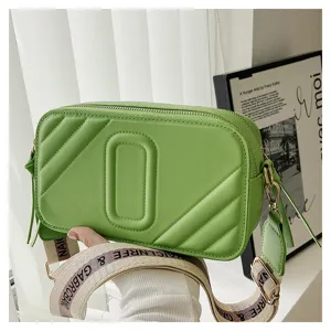 Détail de sac appareil photo vert en cuir matelassé, double fermeture éclair et sangle large.
