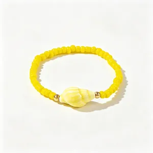 Détail d'un bracelet perles bohème jaune avec un charme de coquillage et billes dorées.