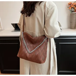 Detailed view of the brown pleated shoulder bag with chain strap worn with trench coat.