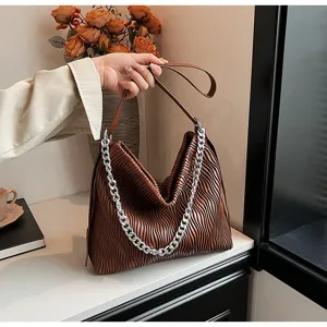 Close-up view of the brown pleated shoulder bag with silver chain detail in a chic indoor setting.