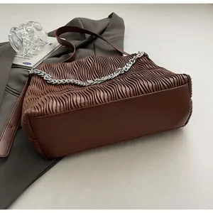 Detailed view of brown pleated shoulder bag with silver chain strap on grey fabric background.
