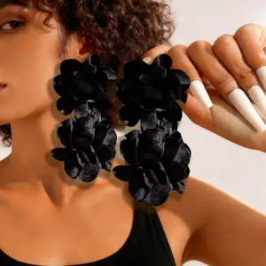 Detailed view of oversized black fabric flower dangle earrings worn by a model
