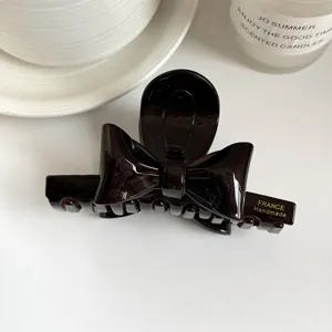 Detailed view of the dark brown acetate hair claw featuring a delicate double-sided stereo bow design.