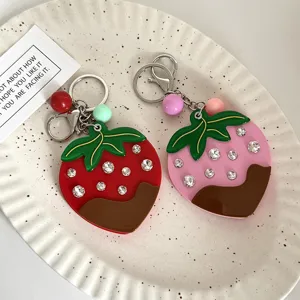 Dettaglio in primo piano di simpatico portachiavi fragola specchietto trucco con strass e cioccolato.