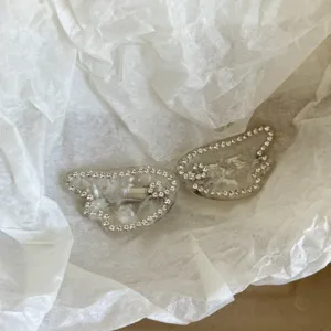 Close-up detail of sparkling rhinestone angel wing hair clips with clear acetate texture.