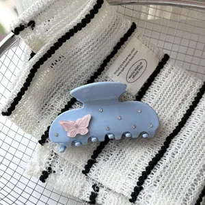 Vue de détail d'une pince à cheveux en acétate bleu clair avec papillon rose et strass brillants.