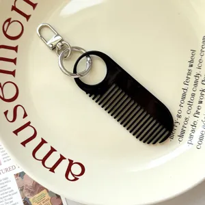 Detail van de zwarte mini kam sleutelhanger met metalen sluiting op het decoratieve bord.