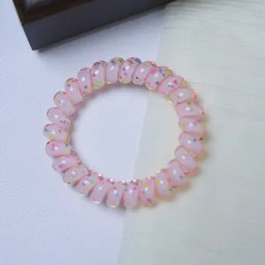 Detailed close-up of a pink transparent telephone cord hair tie with colorful confetti inside.
