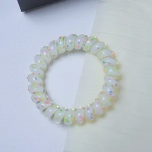 Close-up detail of translucent white telephone wire hair tie with colorful polka dot accents.