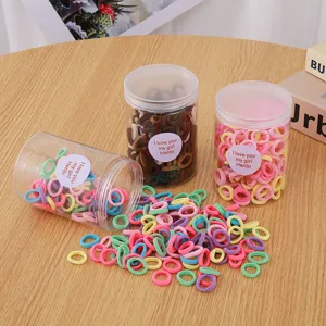 Close up of colorful elastic hair ties packed in clear plastic jars on wooden table detail view.