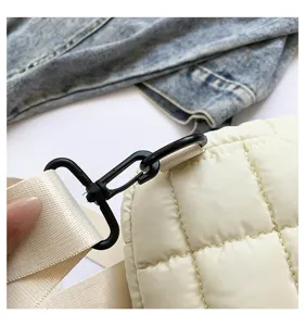 Detail of white quilted puffer crossbody bag with black metal clasp and adjustable strap.